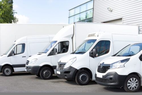 Several cars vans trucks parked in parking lot for rent or delivery